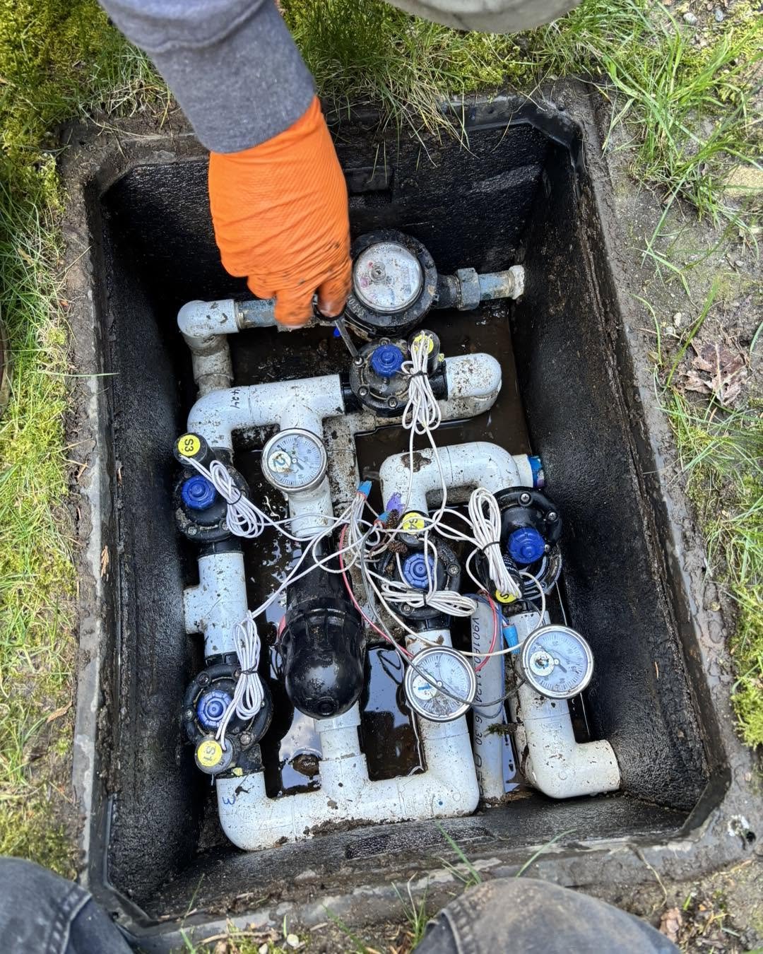 A technician adjusting valves on a pressure-distribution manifold in a ground box.