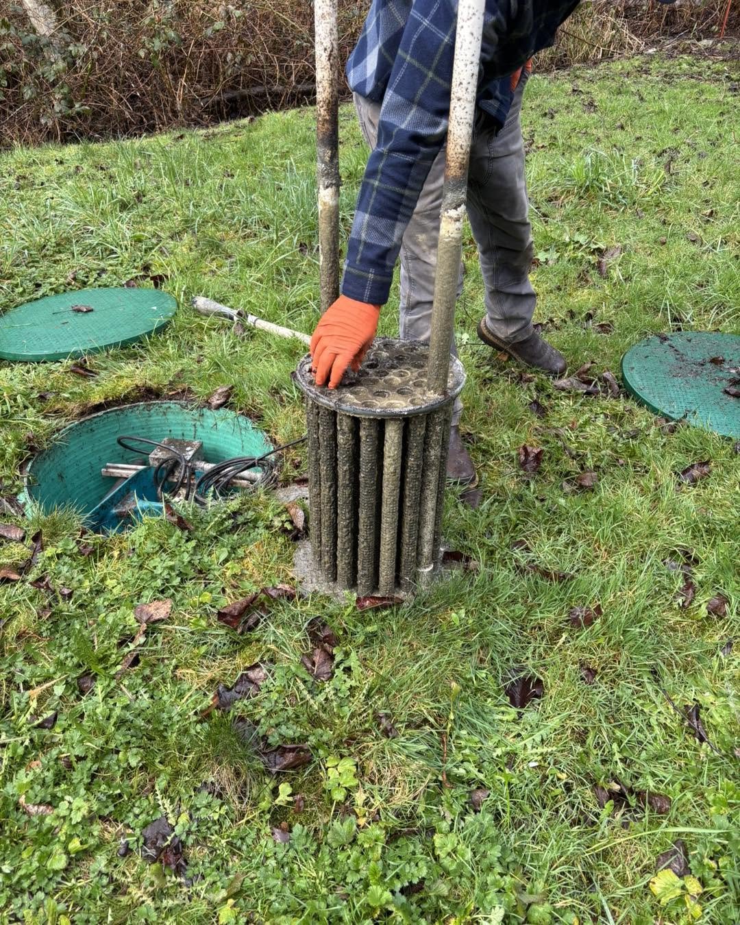 A technician lifting a heavily loaded outlet filter out of an open septic riser.