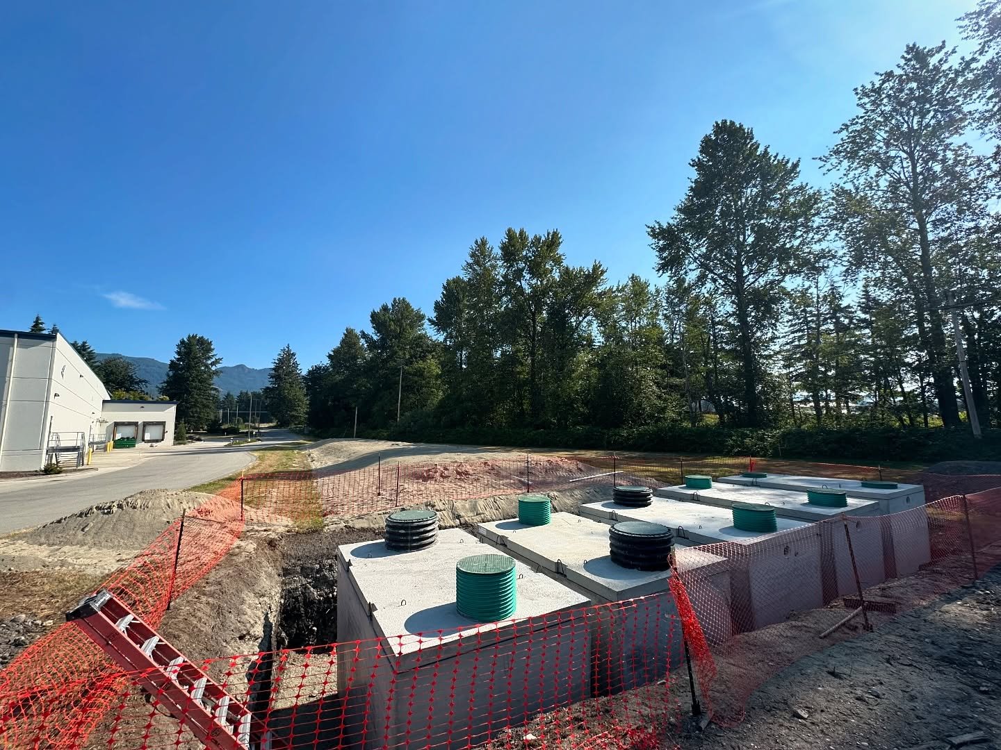 A row of concrete septic tanks with risers set in a large excavation at a commercial site.