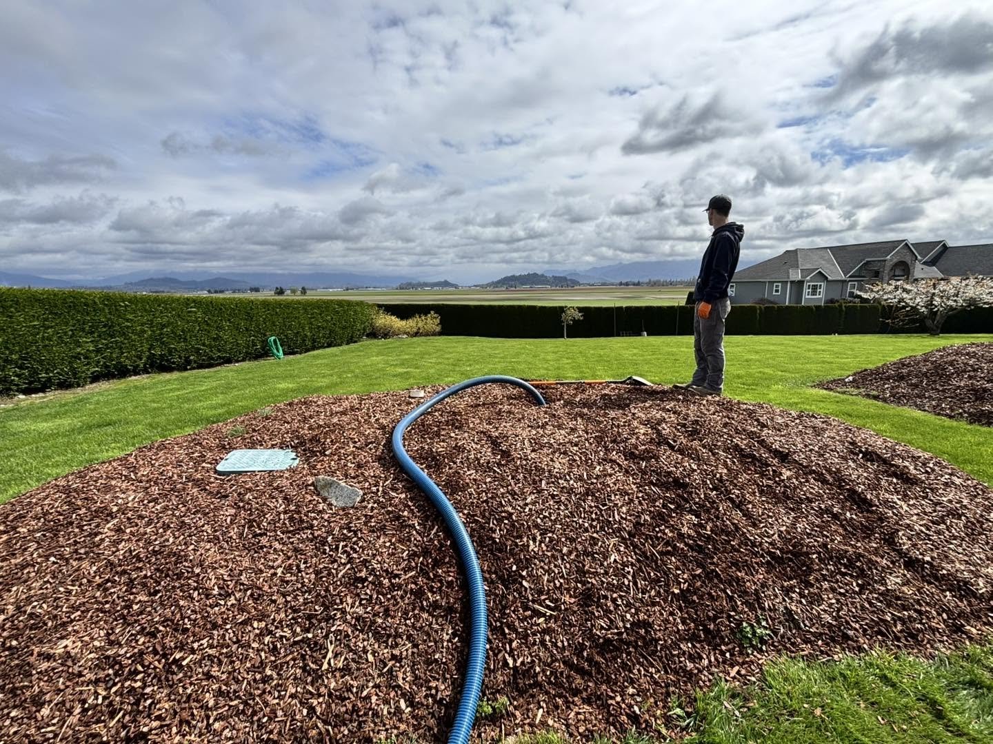 A technician standing on a finished mound system covered in fresh mulch, overlooking farmland.