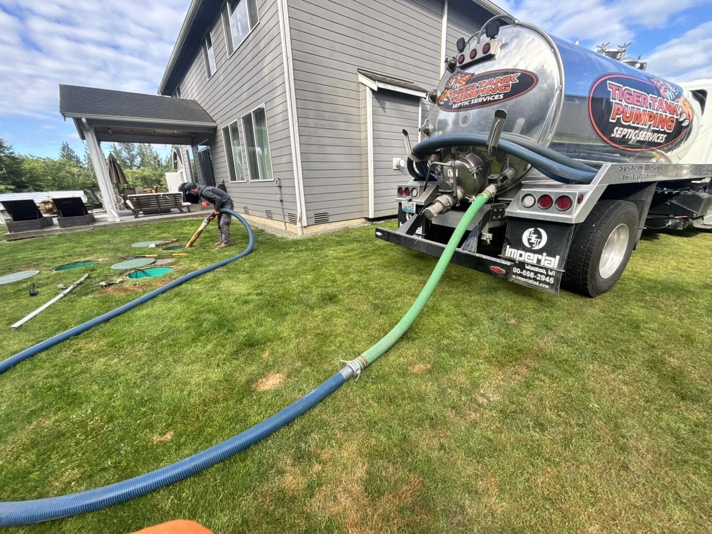A Tiger Tank Pumping truck with hoses run across a lawn to open septic risers.