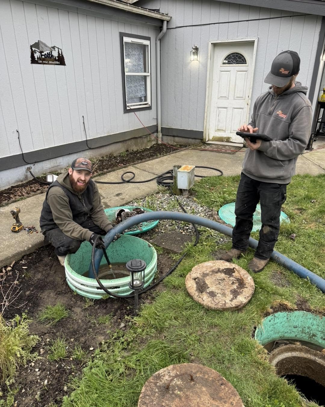 Two Tiger Tank technicians at a pump-out, one working the hose at an open riser and one logging the service on a tablet.