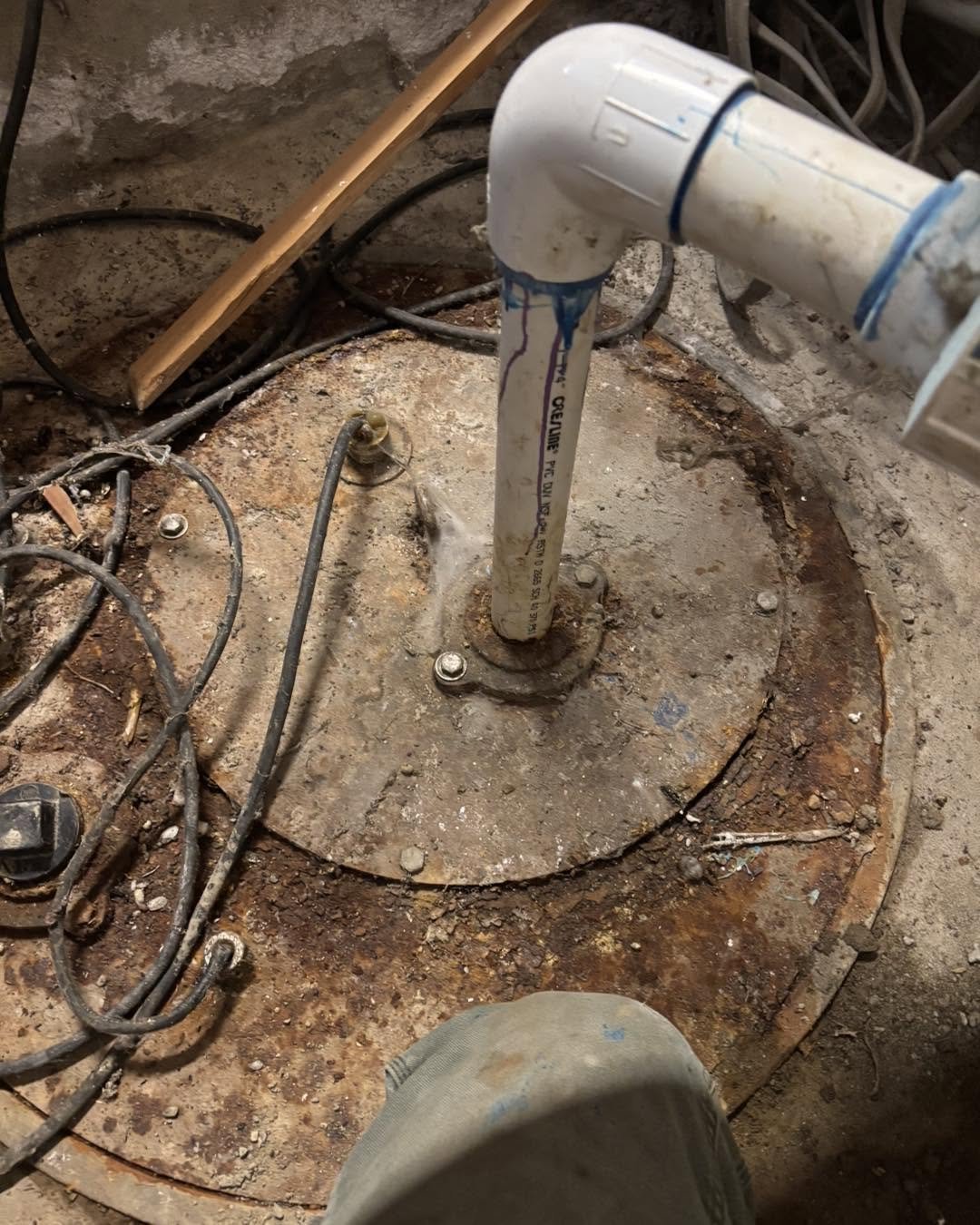 A corroded septic pump vault lid and fittings exposed under a floor.