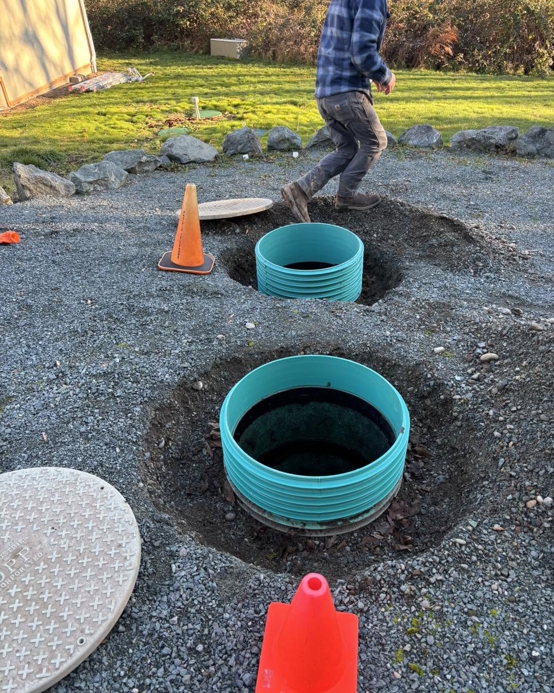 Two new green septic risers installed flush with the gravel grade.
