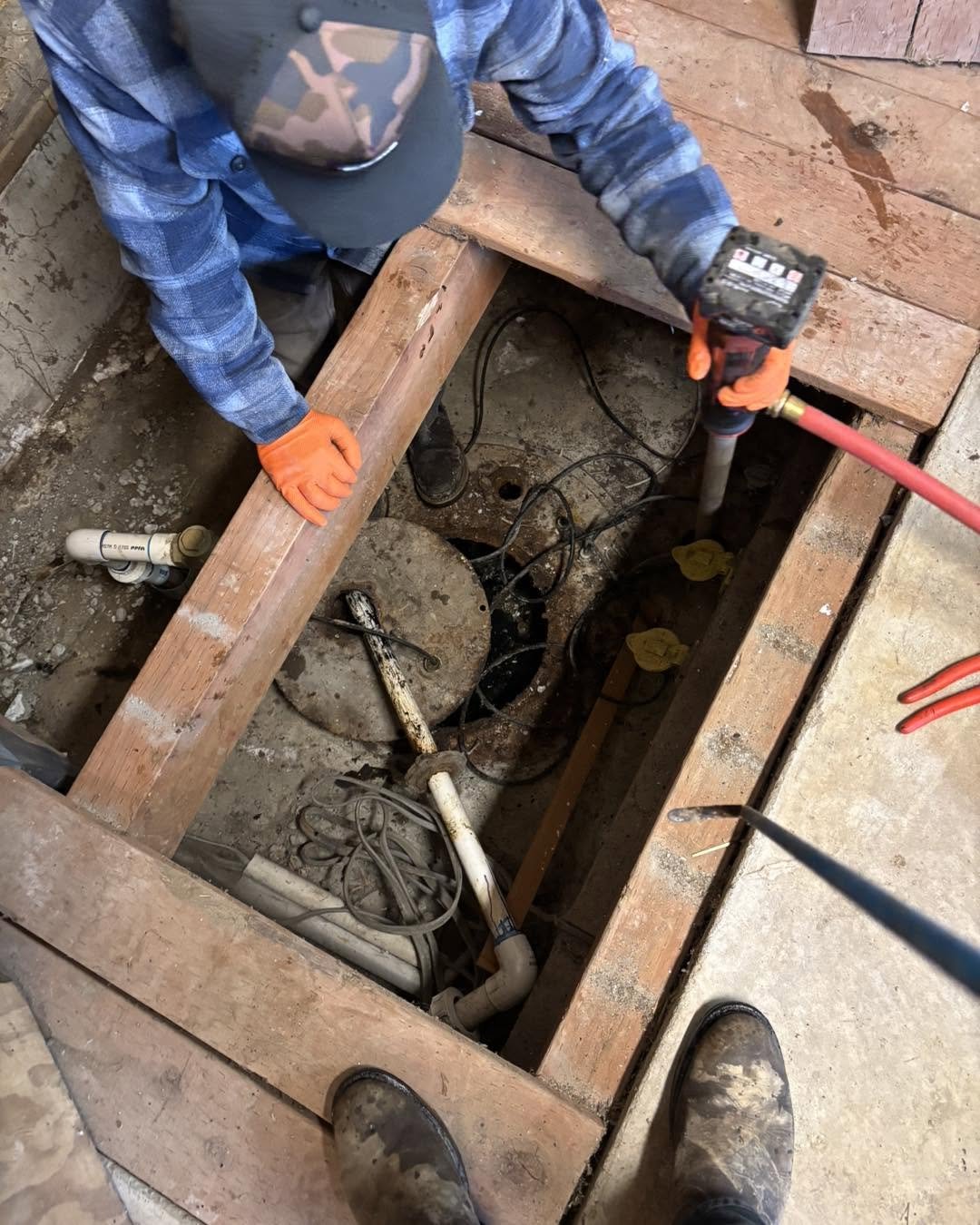 A technician working on septic pump plumbing beneath the floorboards of a house.
